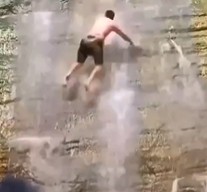Person Falls from Cliff in Background in Front of Waterfall