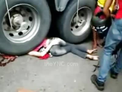 Girl in Tight Jeans and a Pink Shirt lies Underneath Tractor Trailer Giant Wheels